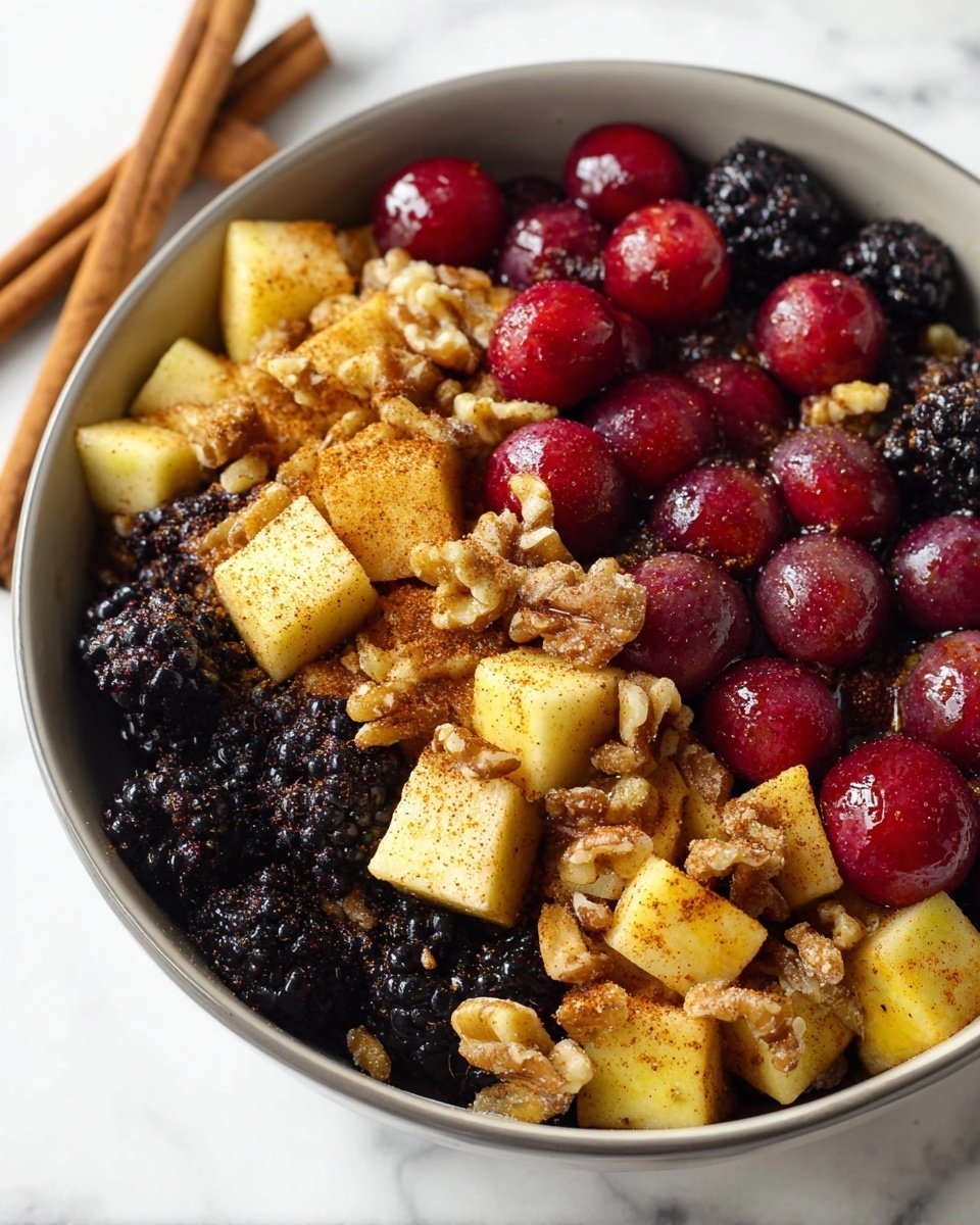 The image shows a close-up of a dish filled with three main layers of ingredients. The bottom layer features shiny dark blackberries spread evenly. The middle layer consists of whole red grapes scattered throughout, adding a round shape and glossy texture. The top layer has chunky yellow apple pieces sprinkled with brown cinnamon powder and mixed with small walnut halves, giving a rough texture. These layers sit in a white bowl placed on a white marbled surface, with two cinnamon sticks visible at the bowl's edge. Photo taken with an iphone --ar 4:5 --v 7